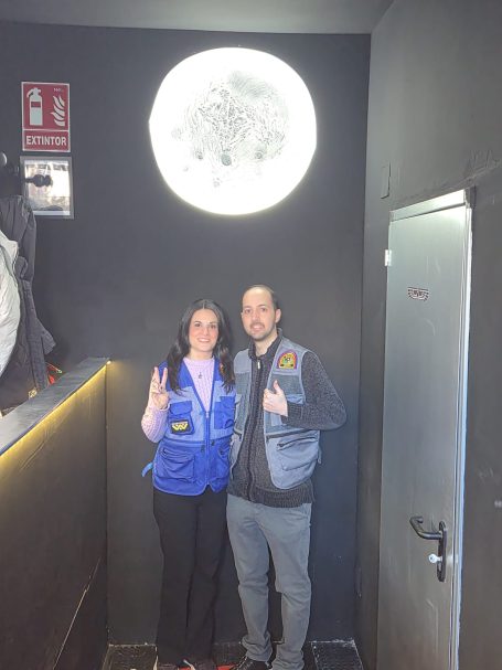 Una pareja posando juntos en una pared negra con una decoración lunar.