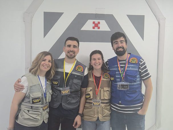 Cuatro personas sonrientes con chalecos, posando frente a un fondo blanco.